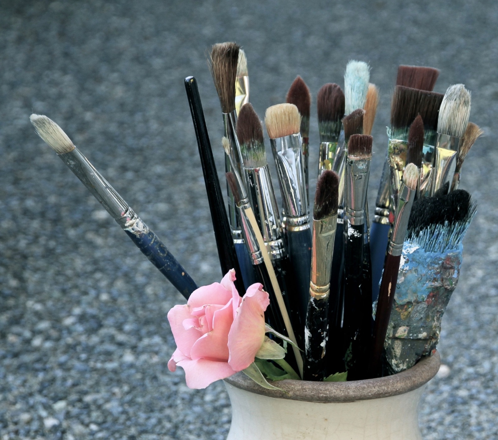 A pot of well-used paintbrushes with a pink rose tucked in front